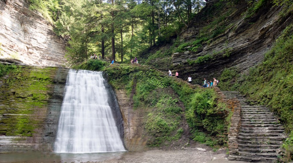 a group of people walking down a steep hill with a waterfall